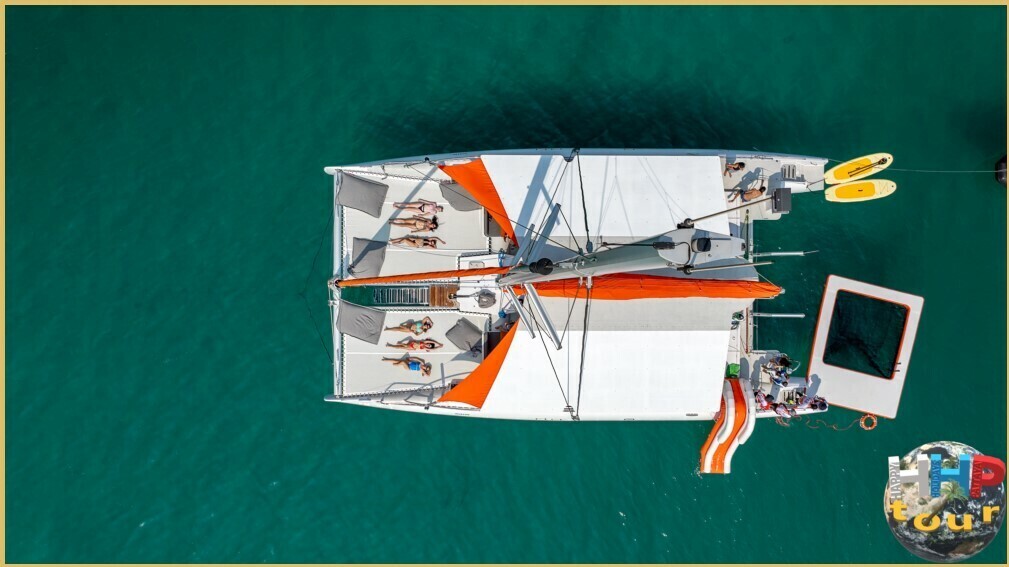 Вид сверху на парусный катамаран Orange Sail. Девушки на загорают на батуте, надувная горка в море и собственный бассейн.